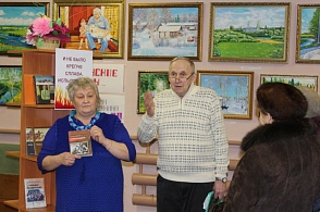 Библиотекарь Наталья Михайловна Севастьянова и Вениамин Александрович Тунгусов у книжной выставки "И не было крепче сплава, испытанного огнем". На заднем плане выставка картин местного художника Владимира Арсентьевича Первышина